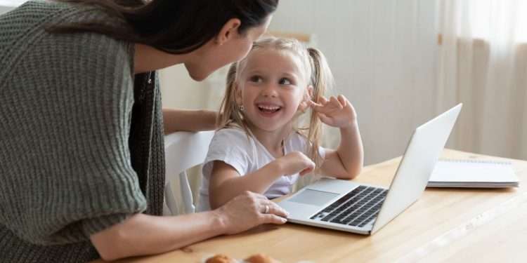 Vemos una madre con su hija pequeña frente a una computadora, en referencia a la implementación de medidas de control parental para iPhone.