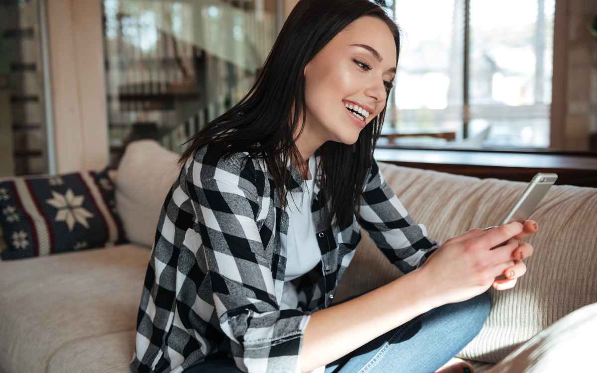 Vemos una imagen de una mujer usando su celular en su casa, en referencia a la consulta cómo ocultar mi red wifi.