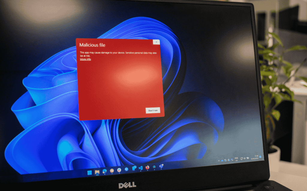 Una computadora portátil muestra una alerta de seguridad en la pantalla con un mensaje en rojo que dice "Malicious file" (Archivo malicioso), advirtiendo sobre el riesgo de dañar el dispositivo o comprometer datos personales sensibles en el ciberespacio.